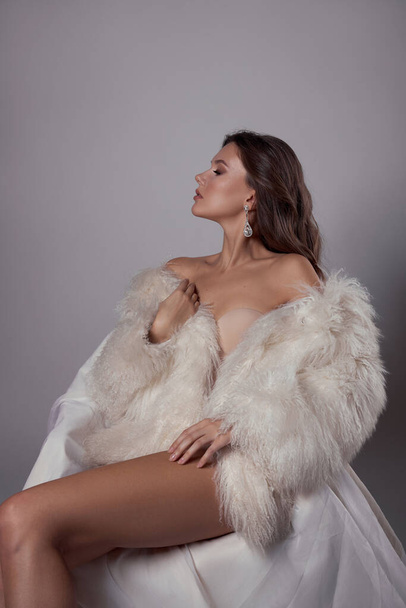 Beauty art portrait of a beautiful woman with long hair, white fur coat with long faux fur. Beautiful earrings in a woman's ears. Hairstyle, hair styling - 写真・画像