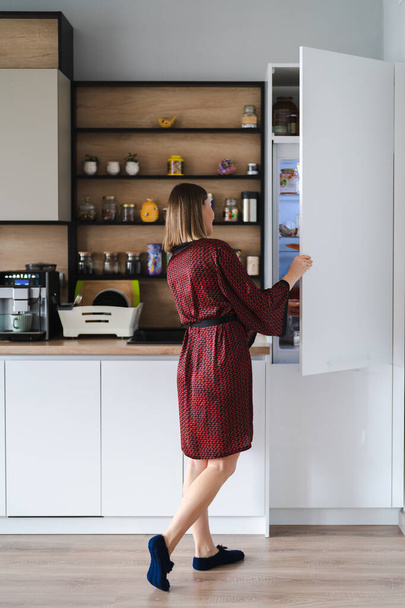 Femme affamée à la recherche de nourriture dans la cuisine du réfrigérateur à la maison - Photo, image