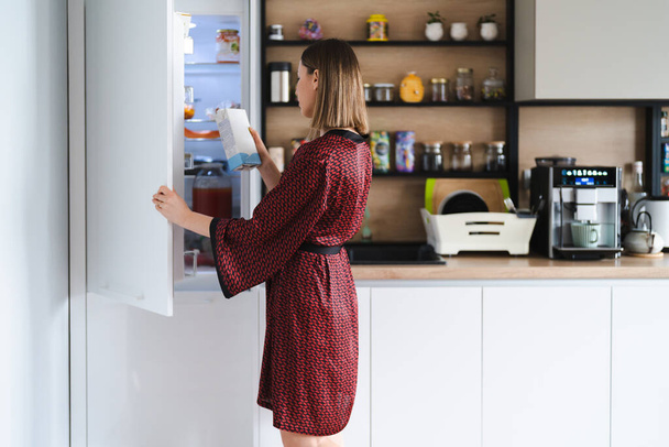 家で冷蔵庫のキッチンで食べ物を探している空腹の女性 - 写真・画像