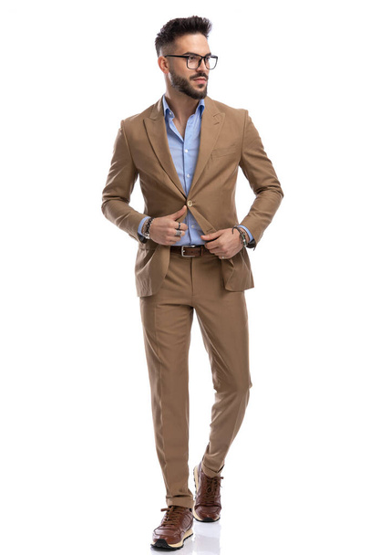 handsome bearded businessman unbuttoning suit, looking to side and walking isolated on white background in studio - Φωτογραφία, εικόνα