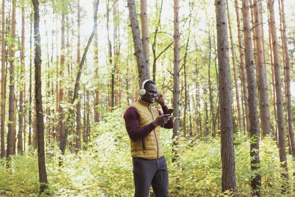 Αφροαμερικάνος ακούει μουσική στο ανοιξιάτικο πάρκο. Έννοια υπηρεσιών Gadget, app και streaming - Φωτογραφία, εικόνα