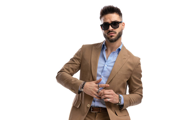 cooler bärtiger Typ im braunen Anzug mit Brille, der Ringe herausnimmt und auf weißem Hintergrund im Studio posiert, Porträt - Foto, Bild