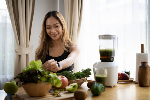 Sorridente donna asiatica che fa verde verdure disintossicazione frullato con frullatore in cucina. - Foto, immagini