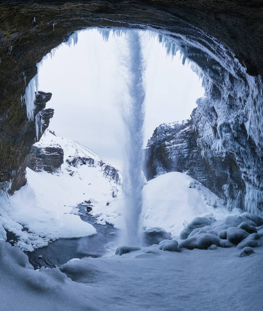 Καταρράκτης Kvernufoss, Ισλανδία. Θέα από το εσωτερικό της σπηλιάς. Ισλανδικό χειμερινό τοπίο. Δυνατό ρυάκι νερού από τον γκρεμό. Ένα δημοφιλές μέρος για να ταξιδέψετε στην Ισλανδία. - Φωτογραφία, εικόνα