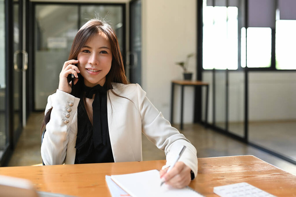 Başarılı iş kadını modern işyerinde oturuyor ve cep telefonuyla konuşuyor.. - Fotoğraf, Görsel