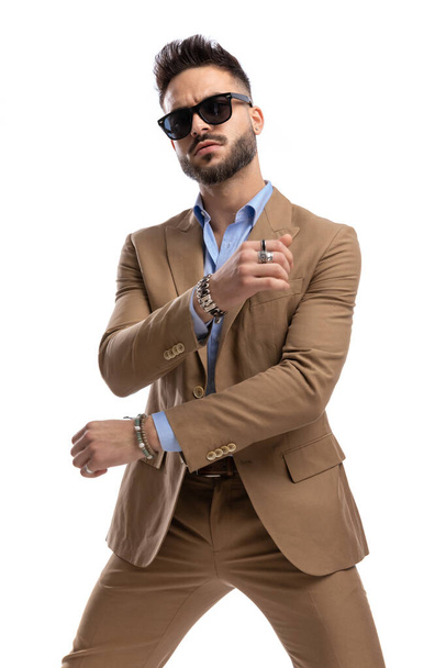 cool fashion guy with sunglasses making hand gesture and dancing on white background in studio - Foto, immagini