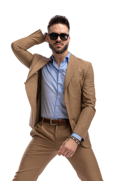 zelfverzekerde man met baard met bril houden hand achter het hoofd en poseren in een mode-manier op een witte achtergrond in de studio - Foto, afbeelding