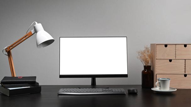 Комп'ютер з порожнім дисплеєм, лампою, книгами та чашкою кави на чорному столі
. - Фото, зображення