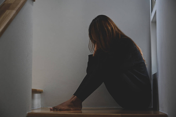 Eenzame jonge vrouw die lijdt aan depressie zit in de donkere kamer. - Foto, afbeelding