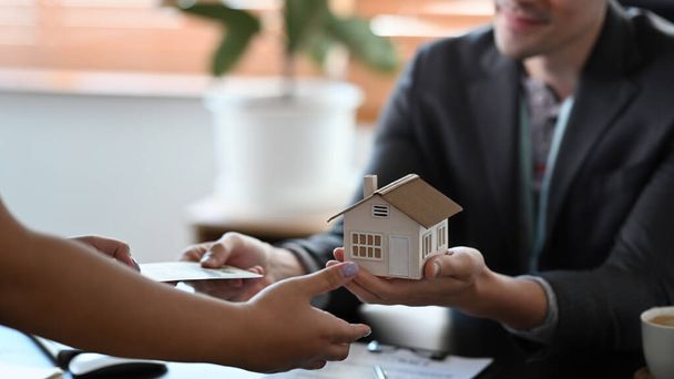 Cropped image of male estate agent holding house model and give proposal to customer. - Photo, Image