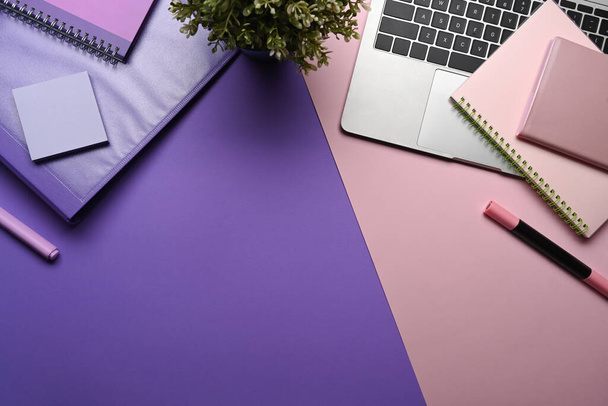 Креативное дизайнерское рабочее пространство с ноутбуком, домашним растением и канцелярскими принадлежностями на фиолетовом фоне. - Фото, изображение