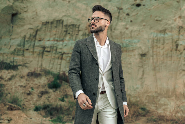 bearded young man with glasses looking to side and having a walk outside in nature while posing - Photo, Image