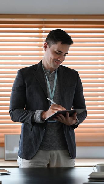 Retrato de empresário atraente em pé no escritório e usando tablet digital. - Foto, Imagem