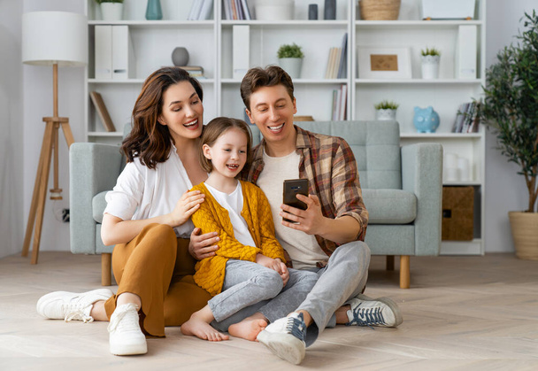 Happy loving family. Young mother, father and daughter using phone. Funny mom, dad and lovely child are having fun staying at home. - Foto, immagini