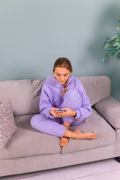 Happy smiling teenage girl with her smartphone browsing social newtwork, communicating relaxed sitting on a sofa at home. Distance online education, study from home concept. - Φωτογραφία, εικόνα