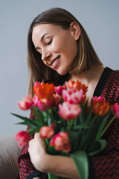 A fiatal nő élvezi a virágokat otthon. - Fotó, kép