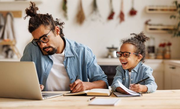 Giovane padre afro-americano che lavora in remoto su laptop con figlio bambino a casa - Foto, immagini