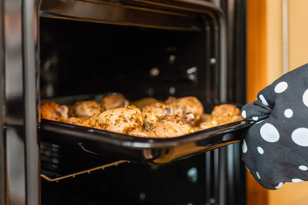 Vrouwenhand trekt gebakken kippenpoten uit de oven. Zachte focus, selectieve focus. - Foto, afbeelding