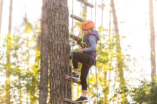Tyttö kiipeily seikkailupuistossa on paikka, joka voi sisältää monenlaisia elementtejä, kuten köysi kiipeily harjoituksia, este kursseja ja zip-linjat
. - Valokuva, kuva