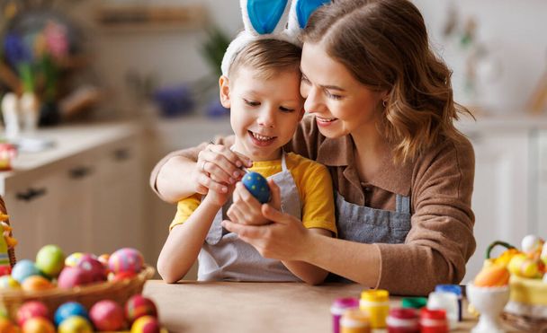 Szerető fiatal anya tanít boldog kisgyerek fia díszíteni húsvéti tojás, miközben ül a konyhában - Fotó, kép
