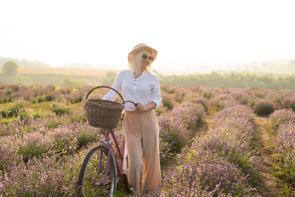 Young blond woman traveller wearing straw hat in lavender field surrounded with lavender flowers. - Foto, Imagen