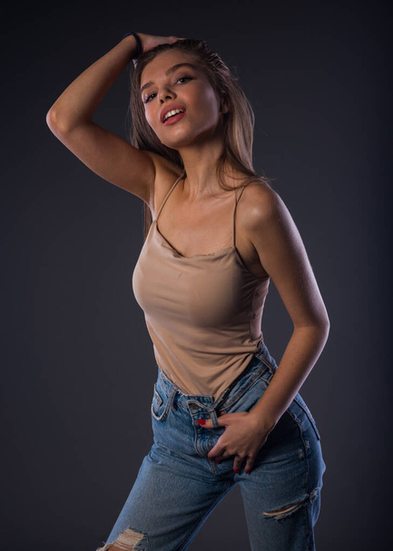 Ελκυστικό γυναικείο μοντέλο ποζάρει σε μπεζ μπλουζάκι και τζιν παντελόνι - Φωτογραφία, εικόνα