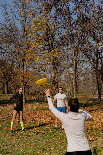 Tre amici attraenti e sorprendenti in forma stanno giocando a frisbee e si divertono insieme nel parco dopo il loro allenamento - Foto, immagini