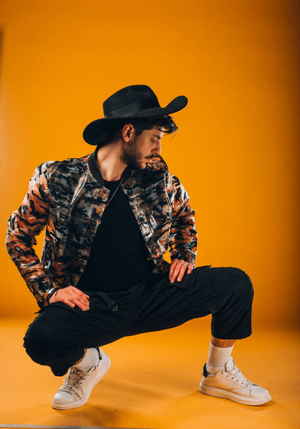 Portrait of a handsome male model with hat posing against orange background - Foto, Imagem