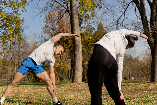 Three attractive and amazing fit friends are warming up and stretching together in the park - Photo, Image
