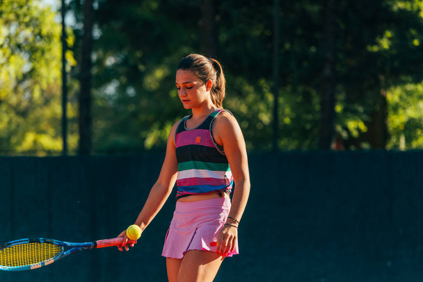 若い女性のテニス選手は、テニスの試合が始まるのを待っている間にラケットで地面にボールを打つ - 写真・画像