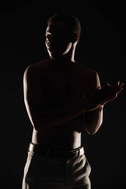 силует чорного чоловіка позує топлес на темному фоні
 - Фото, зображення
