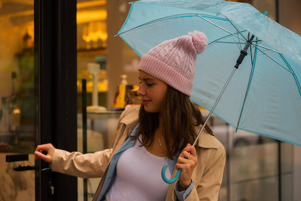 Menina atraente está saindo da loja enquanto segurando seu guarda-chuva fora na chuva - Foto, Imagem