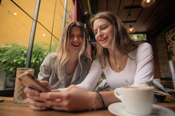 Amazing and attractive two sisters are laughing at something funny on the phone - Photo, Image