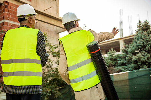 Dois trabalhadores da construção estão de pé na construção, enquanto explica algo, close-up - Foto, Imagem