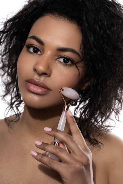 Beautiful black woman with a smooth skin using rose quartz derma roller on white background - Fotografie, Obrázek
