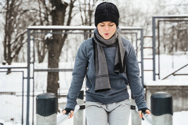 Young athletic woman during her winter outdoor workout on parallel bars - Fotó, kép