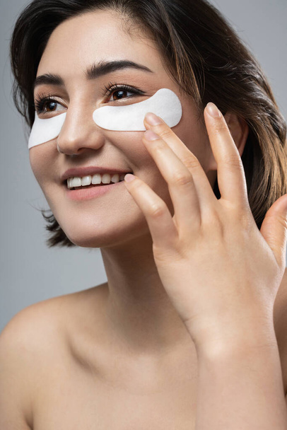 Beautiful brunette woman with a smooth skin applying adhesive under-eyes patches for dark circles  - Fotó, kép