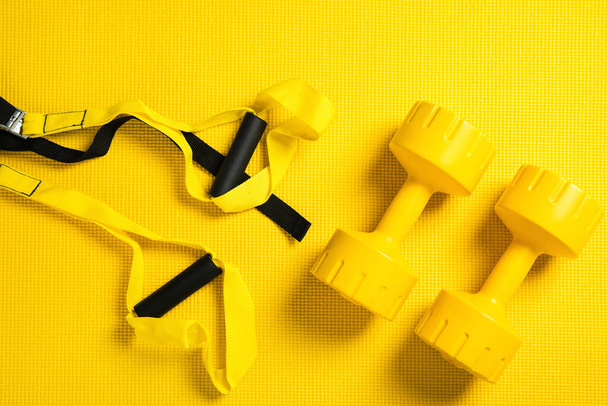 Top view of yellow dumbbells, fitness mat and suspension straps - 写真・画像