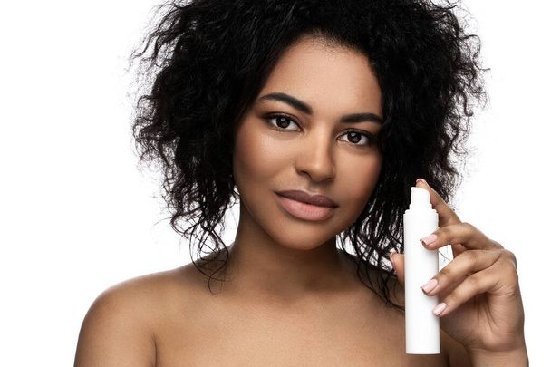 Beautiful black woman with a smooth skin holding bottle of cleansing foam or serum on white background - Foto, imagen