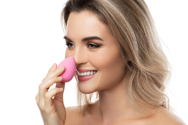 Portrait of beautiful woman with a smooth skin holding makeup sponge on white background - Foto, afbeelding