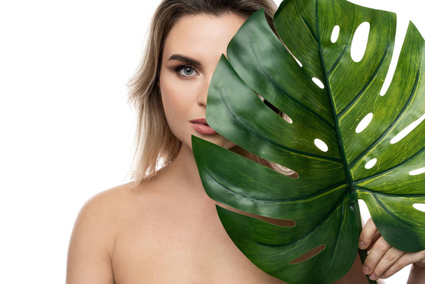 Beautiful caucasian woman with a smooth skin holding green tropical leaf on white background - Фото, изображение