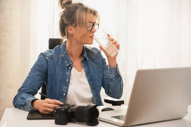 Young woman photographer drinking still water on her workplace - Foto, Bild