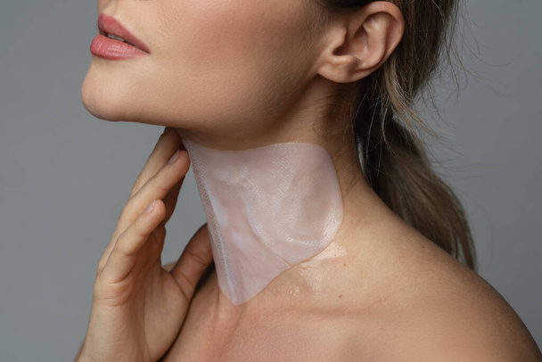 Caucasian woman with a moisturizing and anti aging sheet mask applied on her neck - Foto, Imagem