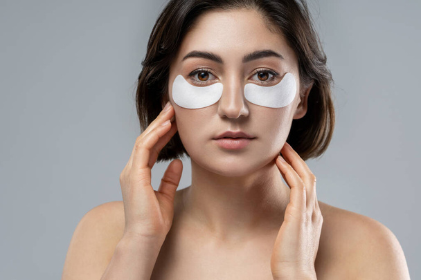 Beautiful brunette woman with a smooth skin applying adhesive under-eyes patches for dark circles  - Photo, Image