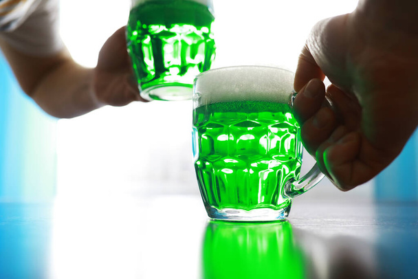 Γιορτές του Αγίου Πατρικίου. Εθνική Ιρλανδική γιορτή. Πράσινη μπύρα. Χέρι με μια κούπα σμαραγδένια μπύρα σε ένα μπαρ. - Φωτογραφία, εικόνα