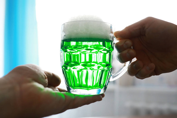 Γιορτές του Αγίου Πατρικίου. Εθνική Ιρλανδική γιορτή. Πράσινη μπύρα. Χέρι με μια κούπα σμαραγδένια μπύρα σε ένα μπαρ. - Φωτογραφία, εικόνα