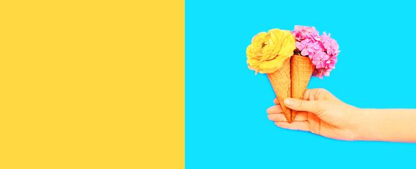 Hand holding cone ice cream with flowers on blue background, blank copy space for advertising text - Фото, изображение