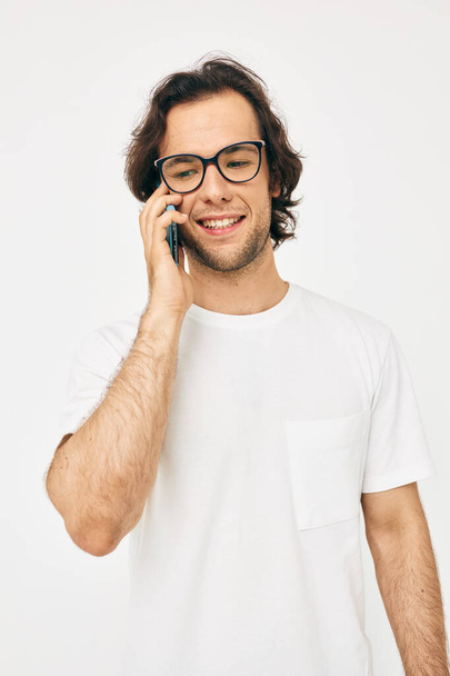 handsome man in a white T-shirt communication by phone light background - Zdjęcie, obraz