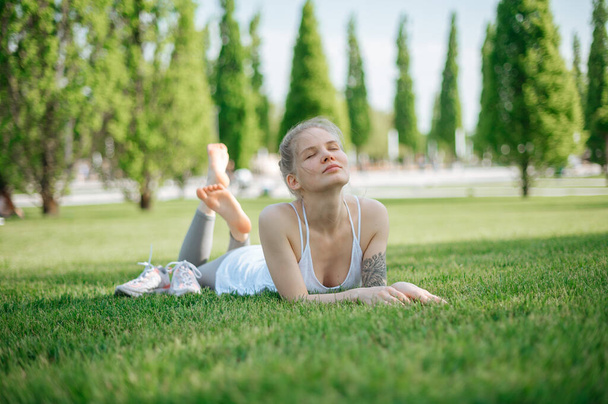 Attractive sportive girl lies on the grass and relaxes in park - Photo, Image