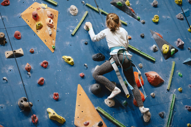 Teenage girl at indoor climbing wall. Kid having fun at bouldering wall. Child learning at climbing class. Sports healthy lifestyle. Youth at climbing summer camp - Photo, Image